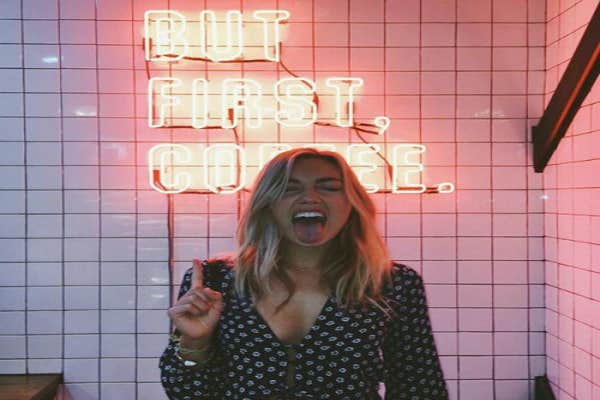 Blonde woman with neon sign behind her.