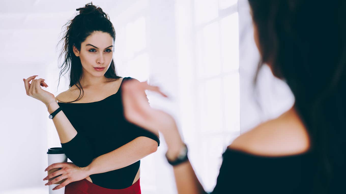 Brunette girl in tracksuit looking at mirror satisfied with body shape