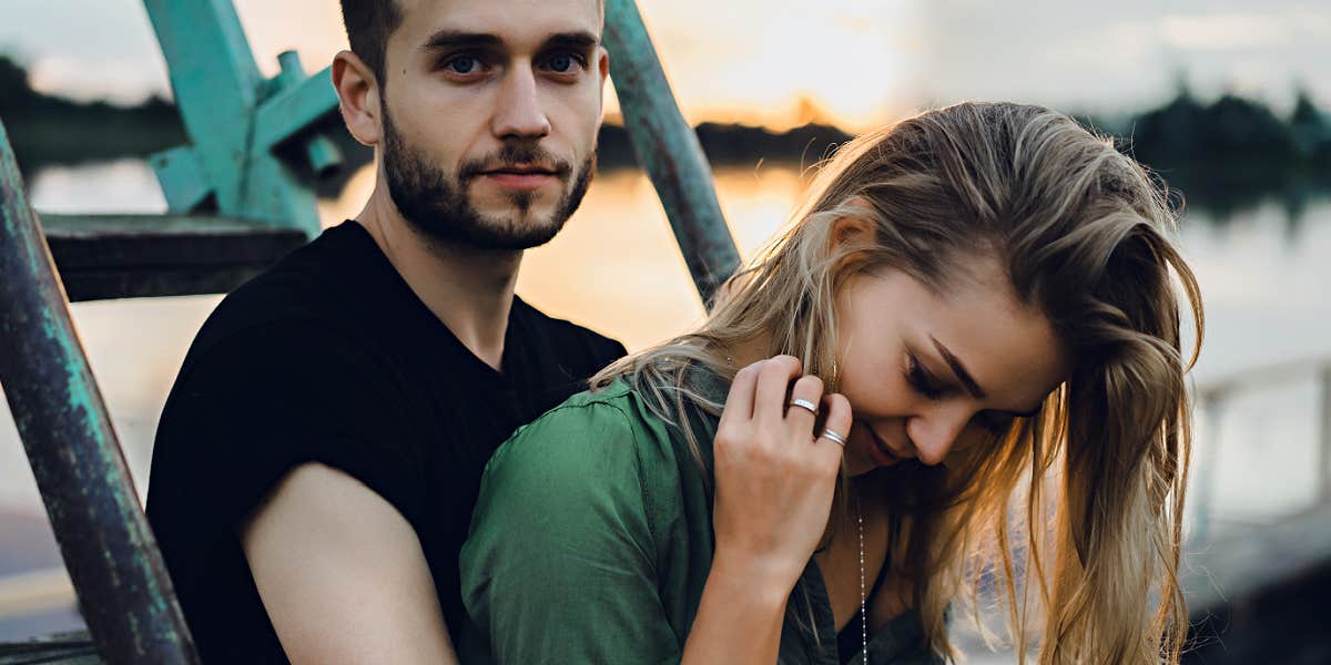 couple sits on a ladder on a pier or wharf, she looks down, he looks at camera