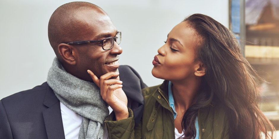 Woman holds a mans chin in her hands as she makes a kissing face