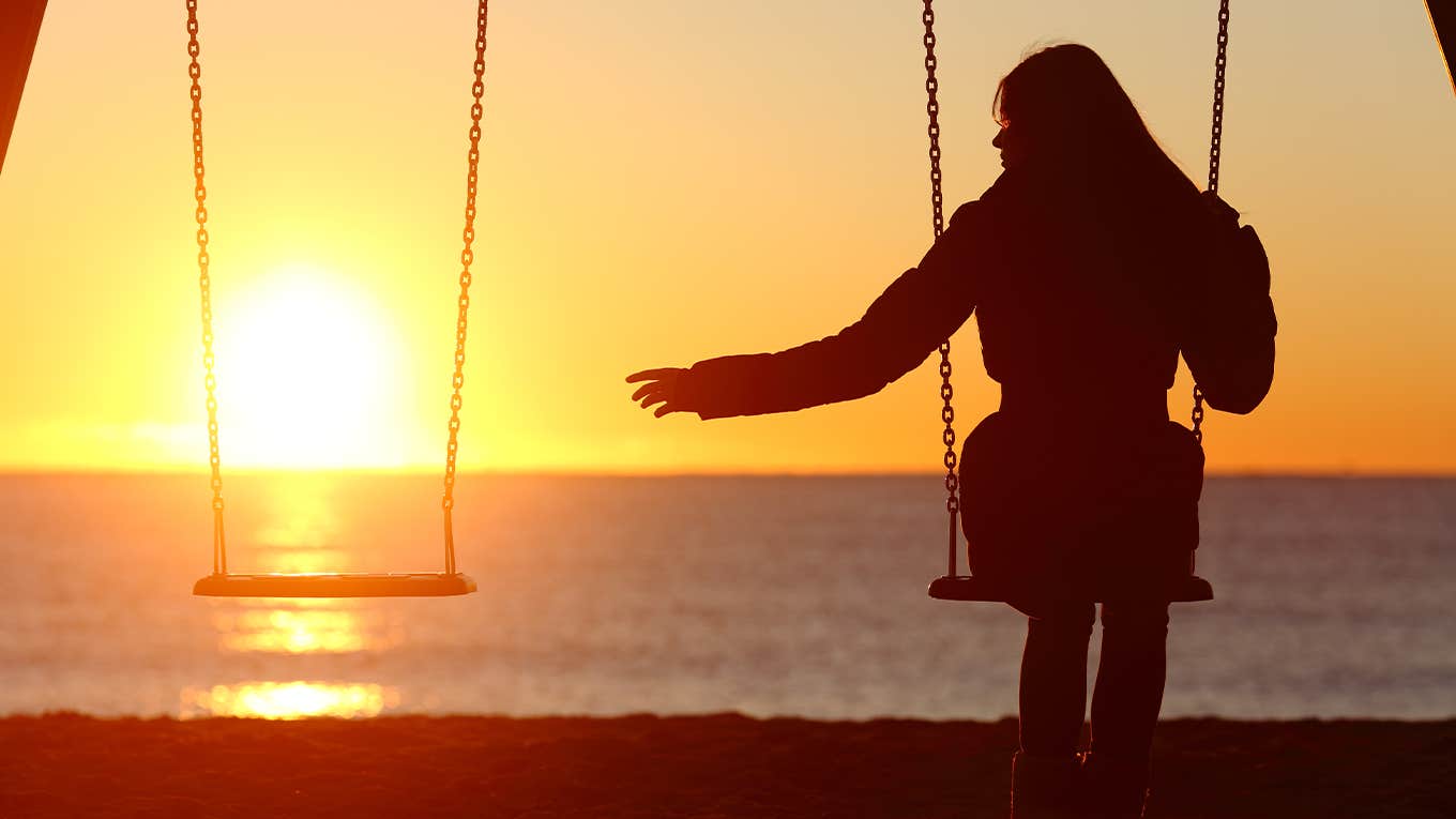 Single or divorced woman alone missing a boyfriend while swinging on the beach at sunset