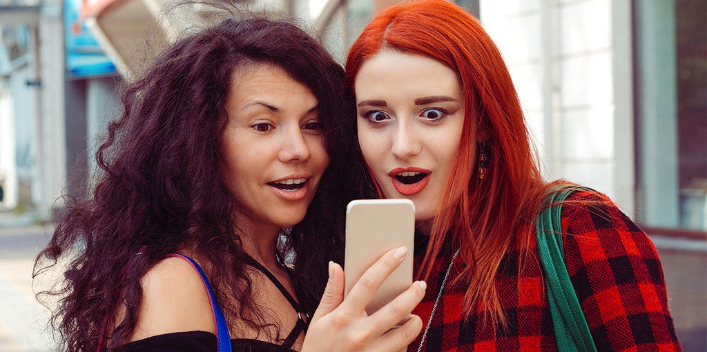 Two young women looking at a phone in shock Two young women looking at a phone in shock