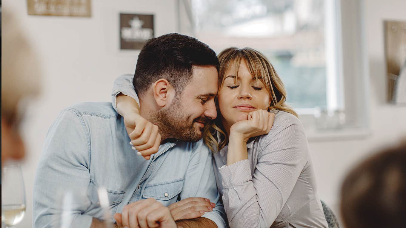 Affectionate woman embracing her husband while sitting at dining table.