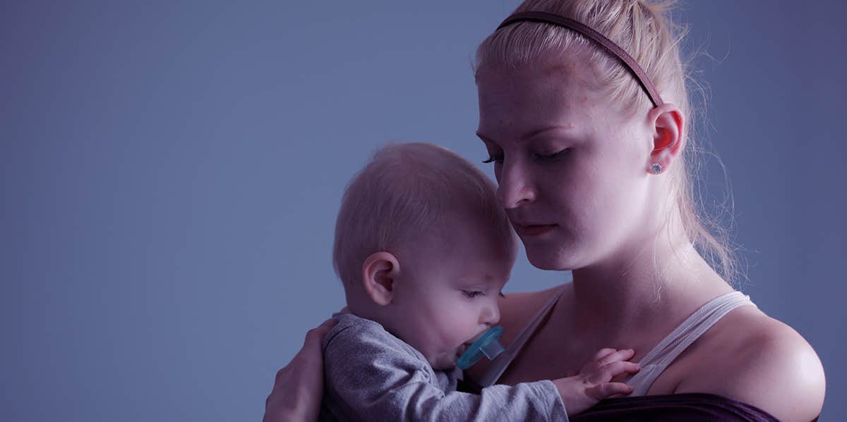 A photograph of a mom with a pensive expression as she holds her child.