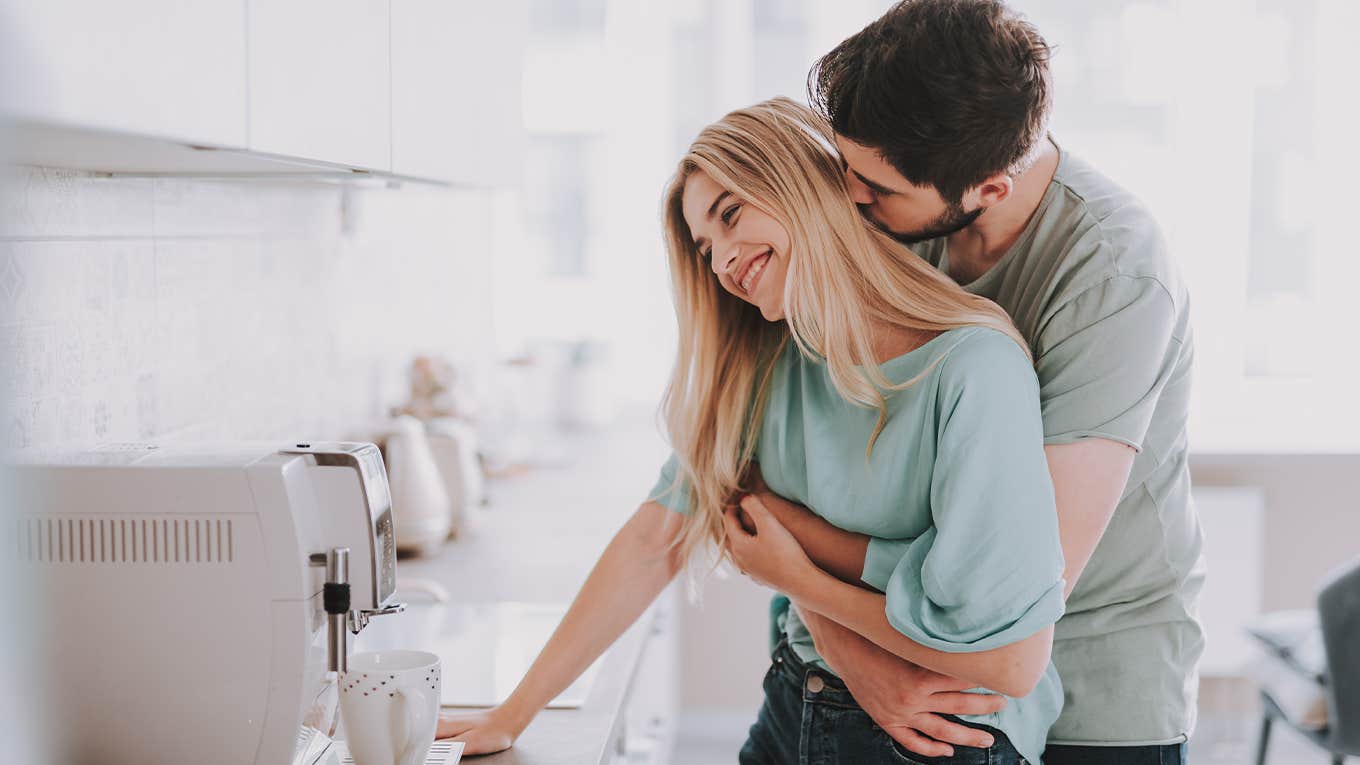 Bearded guy standing behind attractive blonde girl and kissing her. They are waiting for hot drink