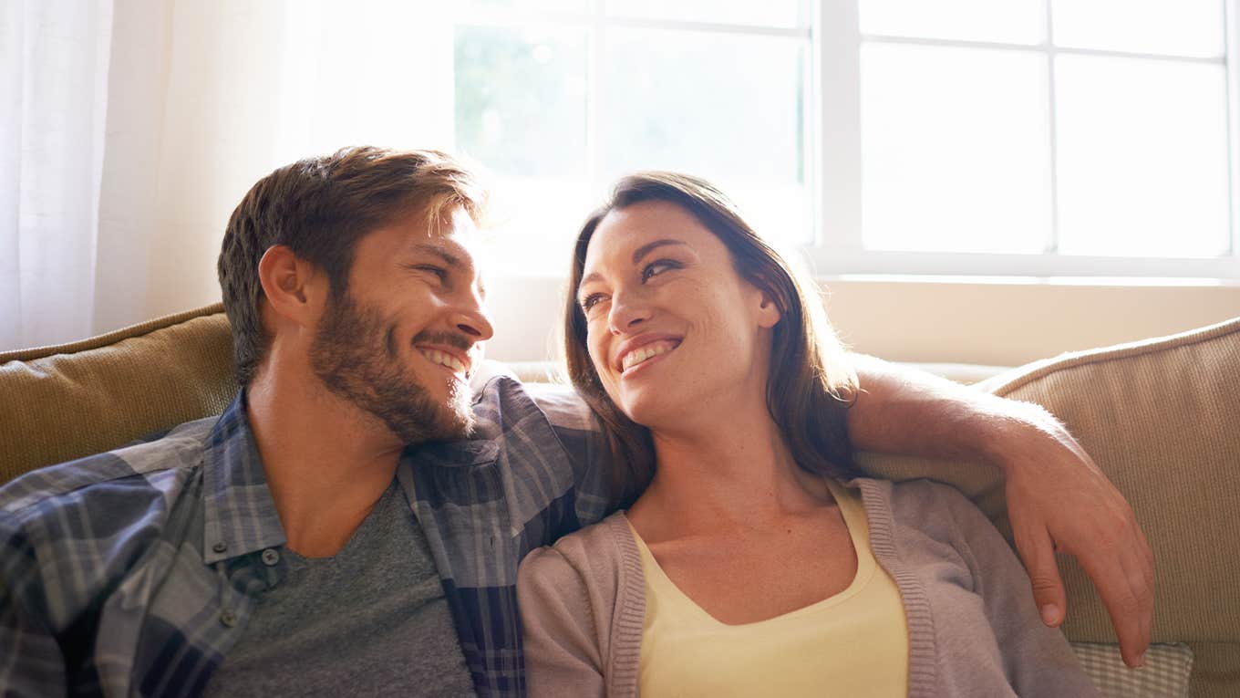 Couple, love and hug or smile at each other on a couch