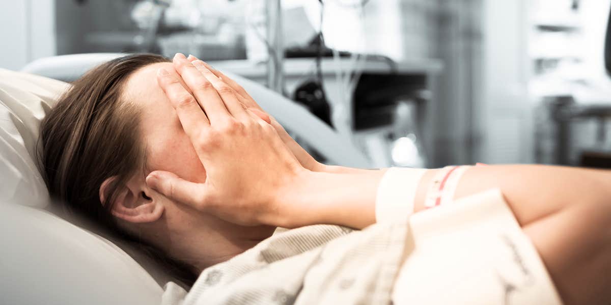 woman lying in hospital bed with hands over face