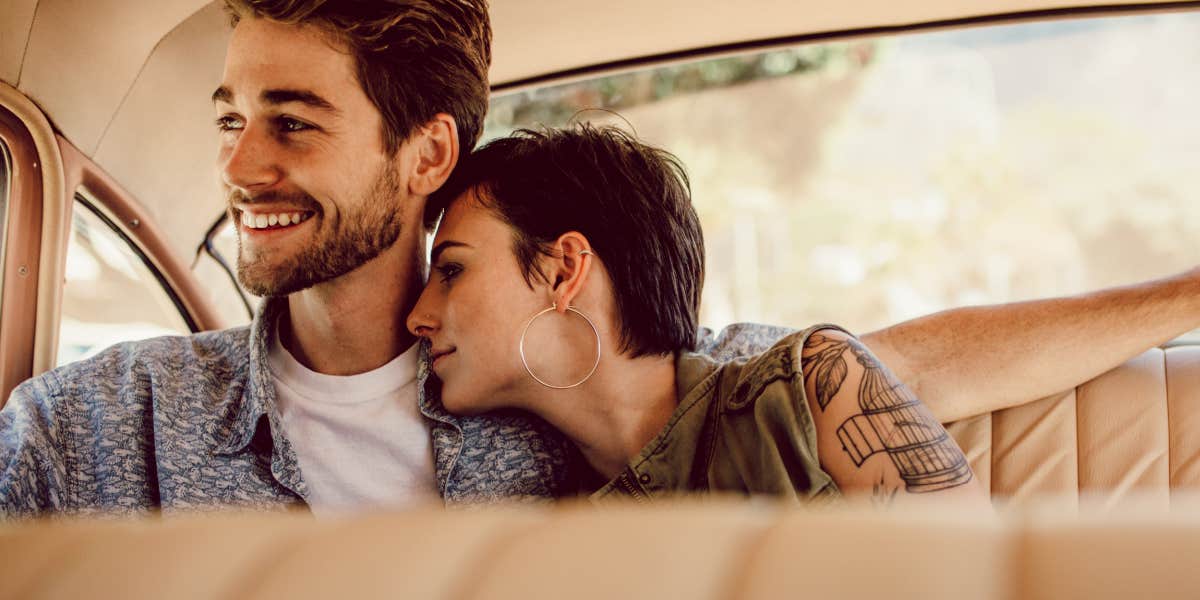 woman and man in classic car, woman with tattoos, man with beard, lovingly sitting together