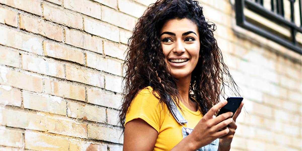 lovely young woman with curly hair smiles against a brick wall