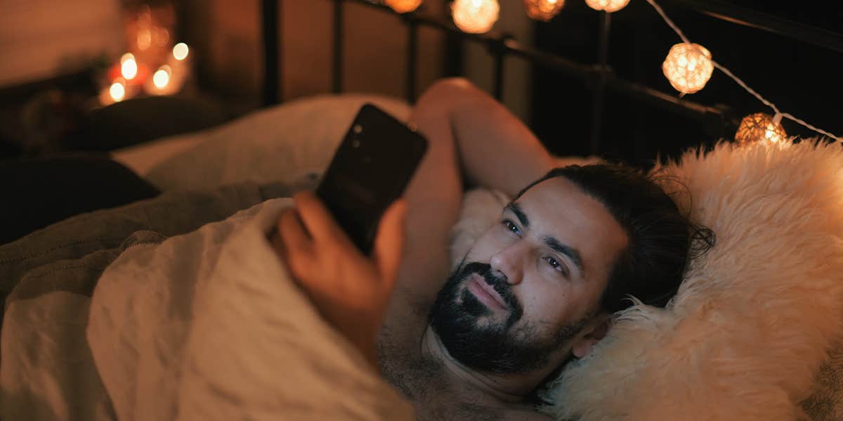 man looking at phone while laying in bed at night
