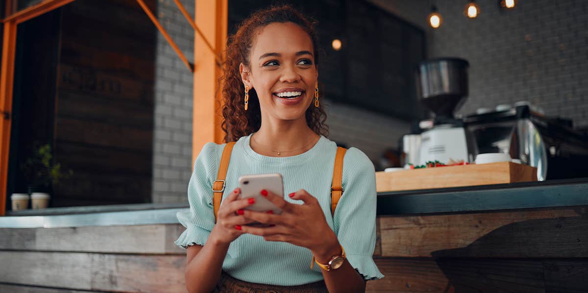 The Amazing Secret To Minding Your Own Business happy woman sitting at coffee shop holding phone