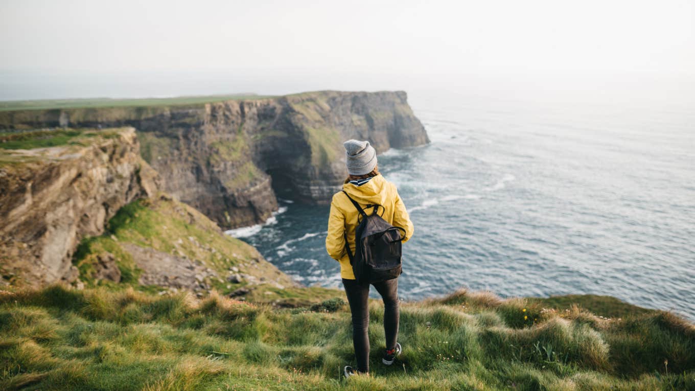 woman admires view from cliff by the ocean