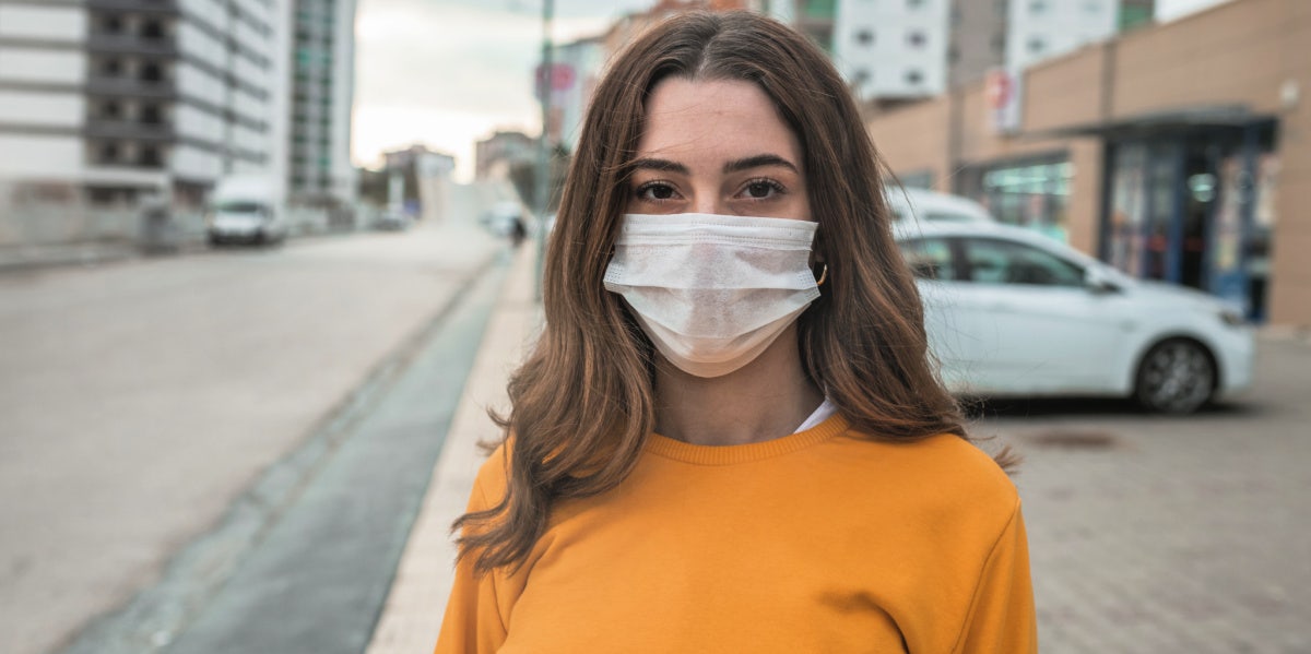 woman in yellow shirt wearing covid mask outside