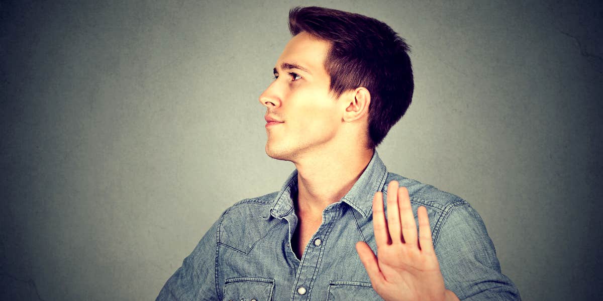 man with head to the side holding up hand to the camera