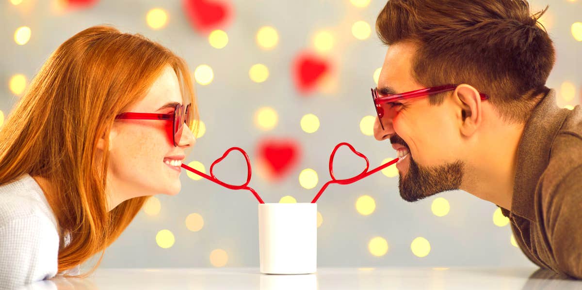 Are Women More Romantic Than Men? Science Answers woman and man wearing heart glasses and sharing a drink through straws