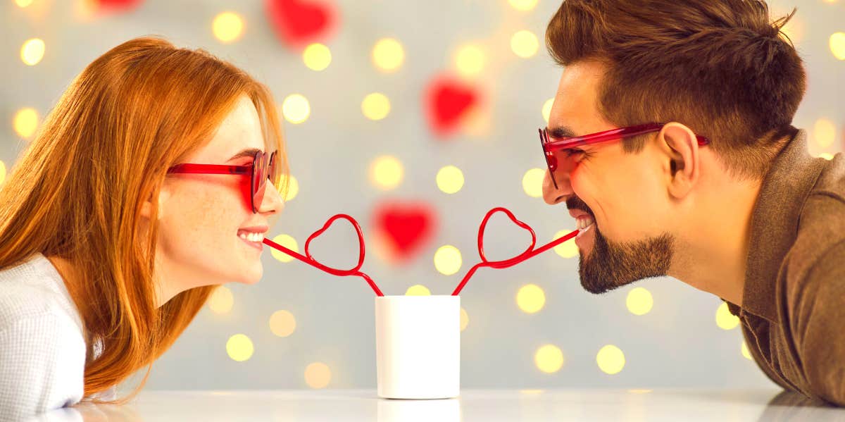 woman and man wearing heart glasses and sharing a drink through straws