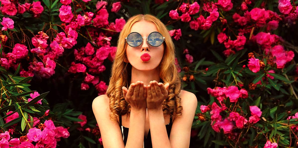 woman blowing kiss in front of pink flower bushes