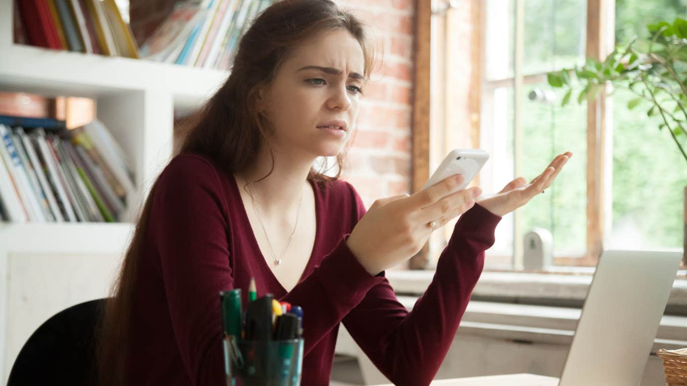 frustrated woman looking at phone sitting at computer