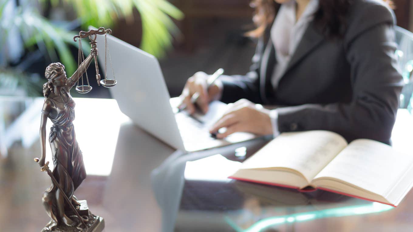 attorney working at desk on laptop with statue of justice