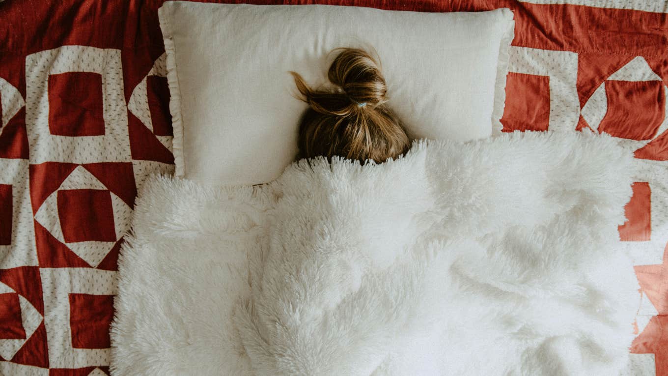 Sleep Expert Shares Austrian Trick For Getting A Good Night's Rest woman sleeping under blanket on bed