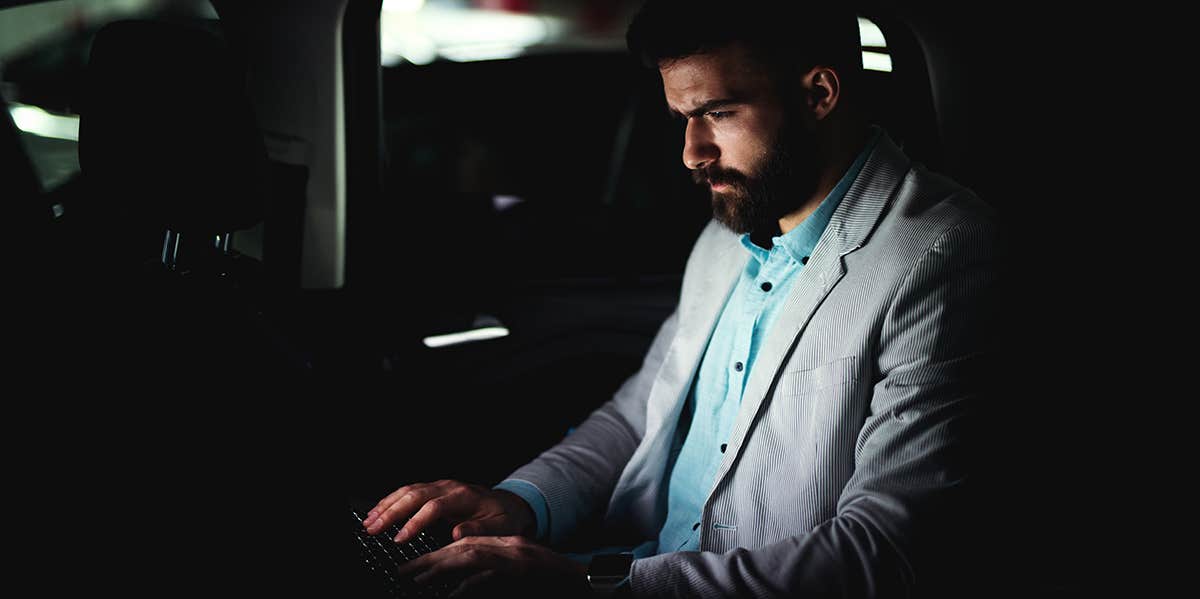 guy typing on laptop doing work at night in back of car