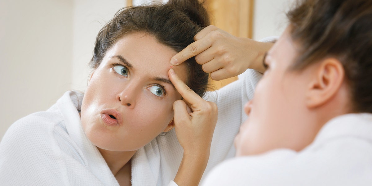 woman popping a pimple in the mirror