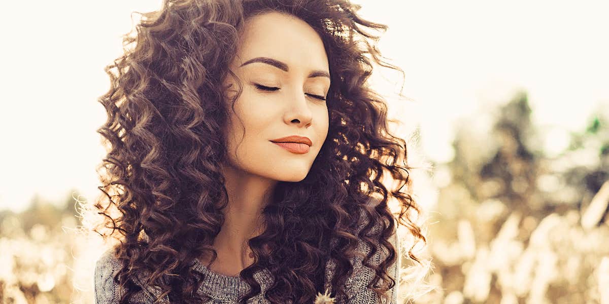 lovely woman with curly brown hair looks peaceful in a field