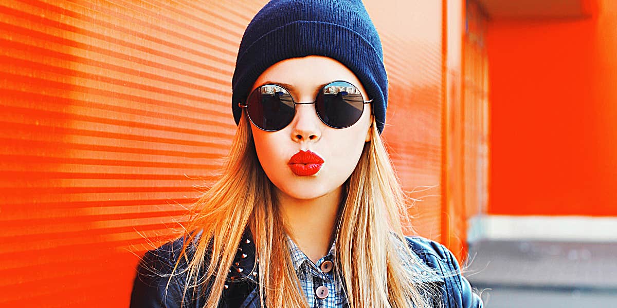 woman with red lips does a kiss face, standing in front of a red and orange corrugated wall