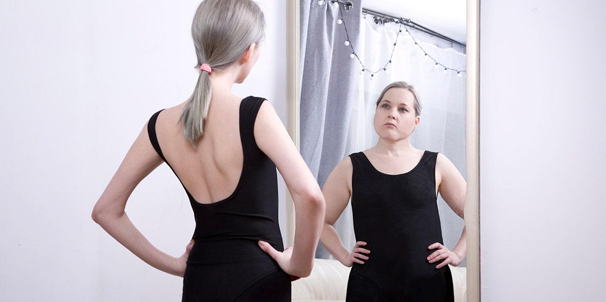 skinny woman looking in mirror at larger version of herself