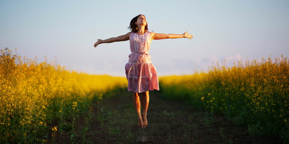 woman jumping in a yellow field, wearing a pink dress