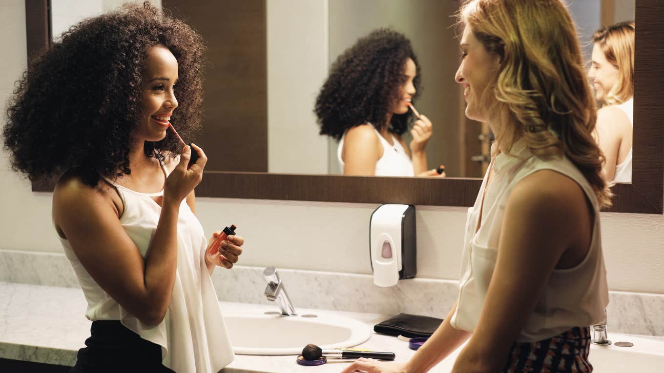 Why Bonding Over Hating The Same Things Creates Closer Friendships two women gossiping in a bathroom