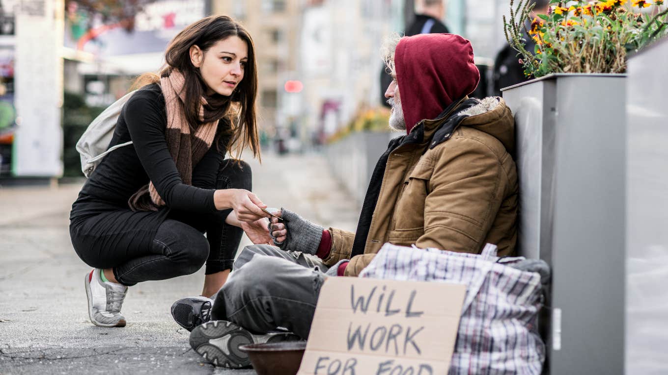 woman kneeling to help homeless man