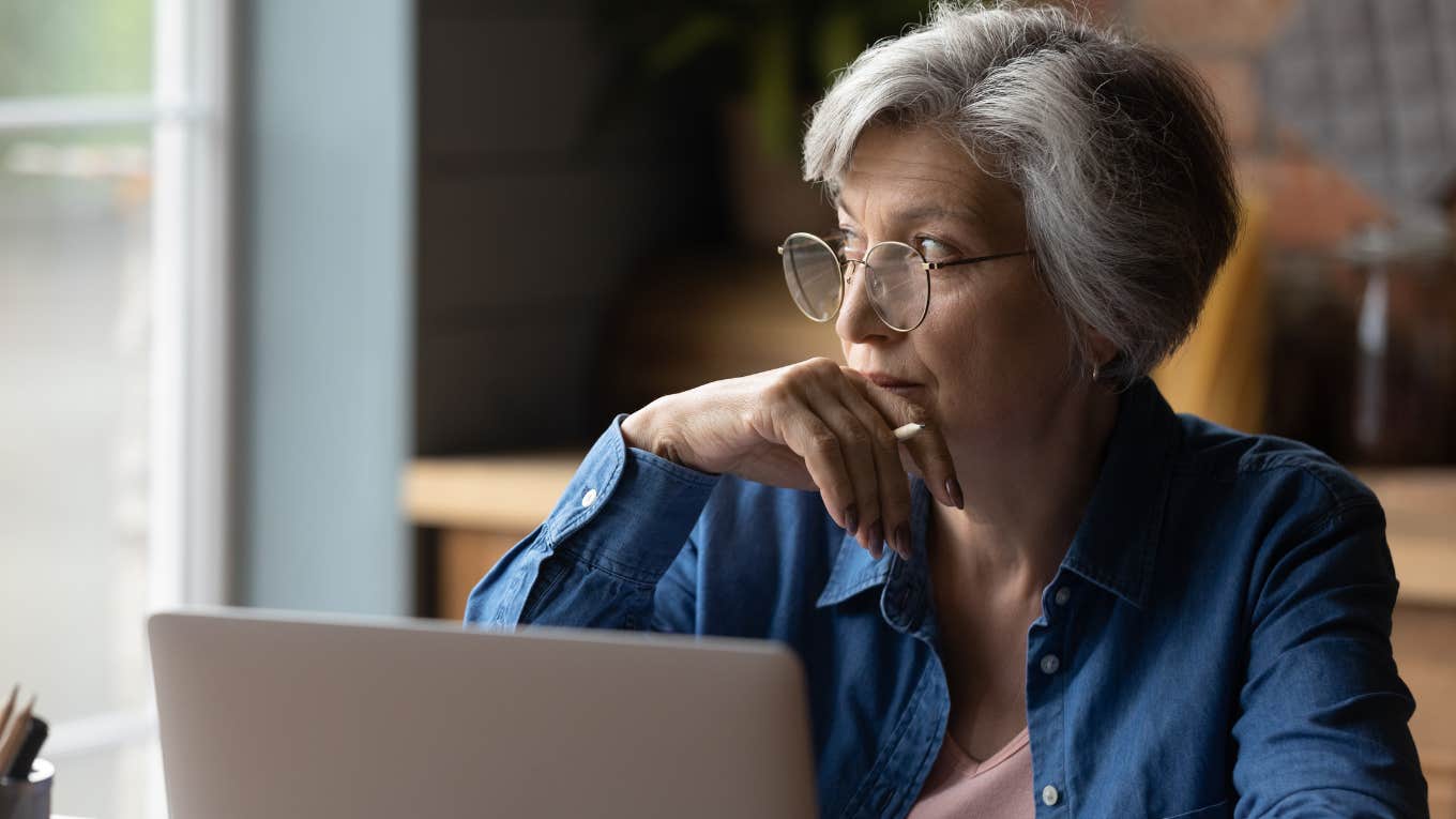 Boomers Admit They Don't Want To Retire Because They Like Going To Work older woman looking out window with laptop in front of her sitting at table