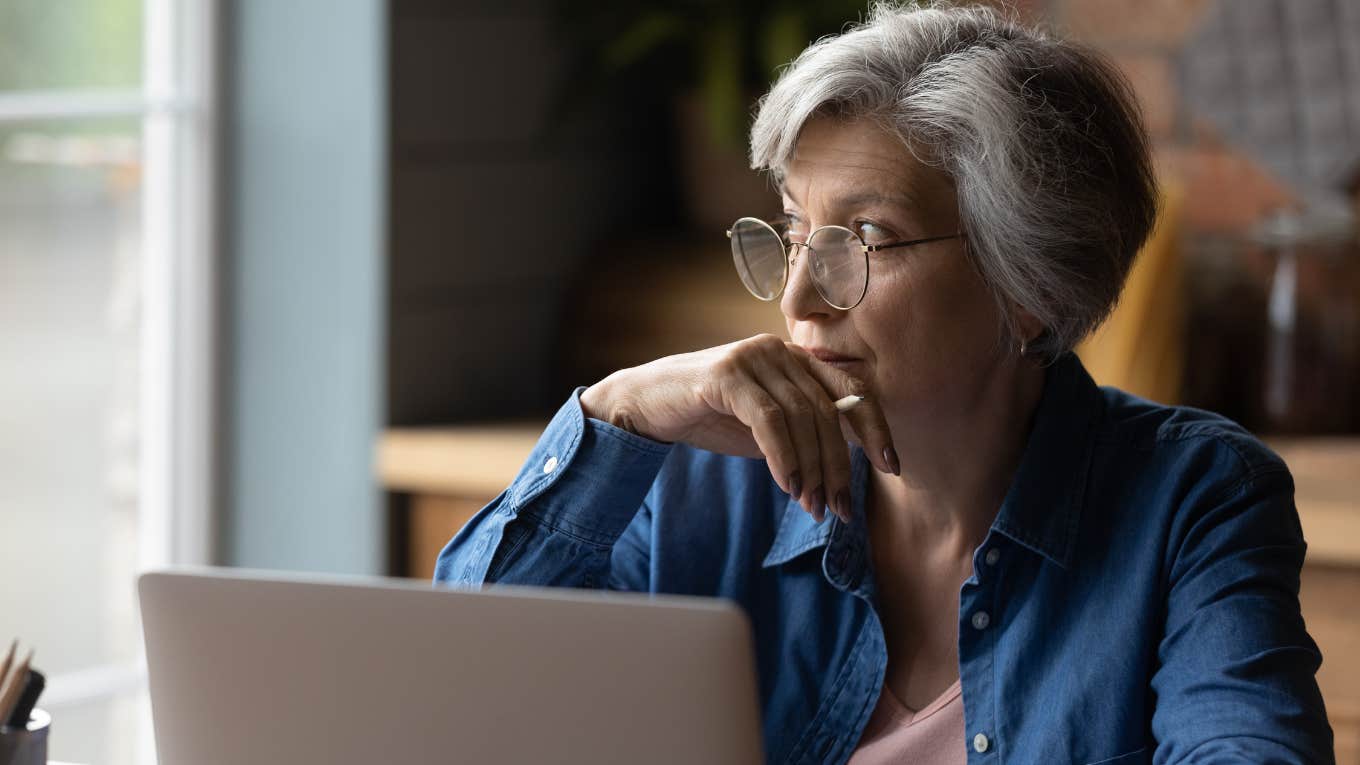 older woman looking out window with laptop in front of her sitting at table