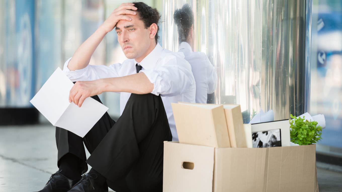 frustrated employee sitting on floor with boxes and paper in hand after being laid off