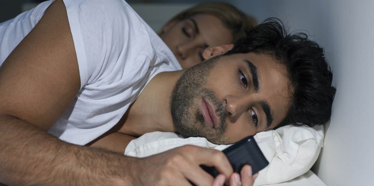 Man texting someone while his partner sleeps