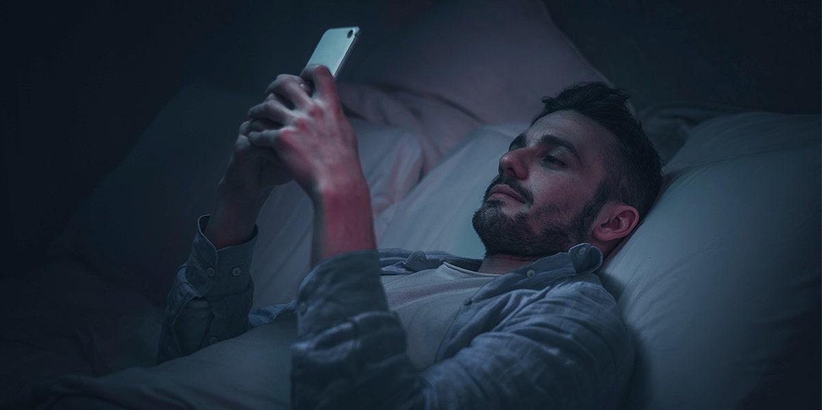 man laying in bed at night looking at phone