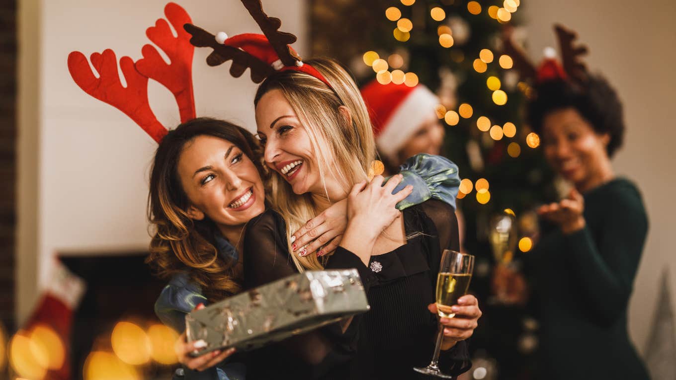 smiling friends huging and giving presents to each other while gathering at home to celebrate Christmas