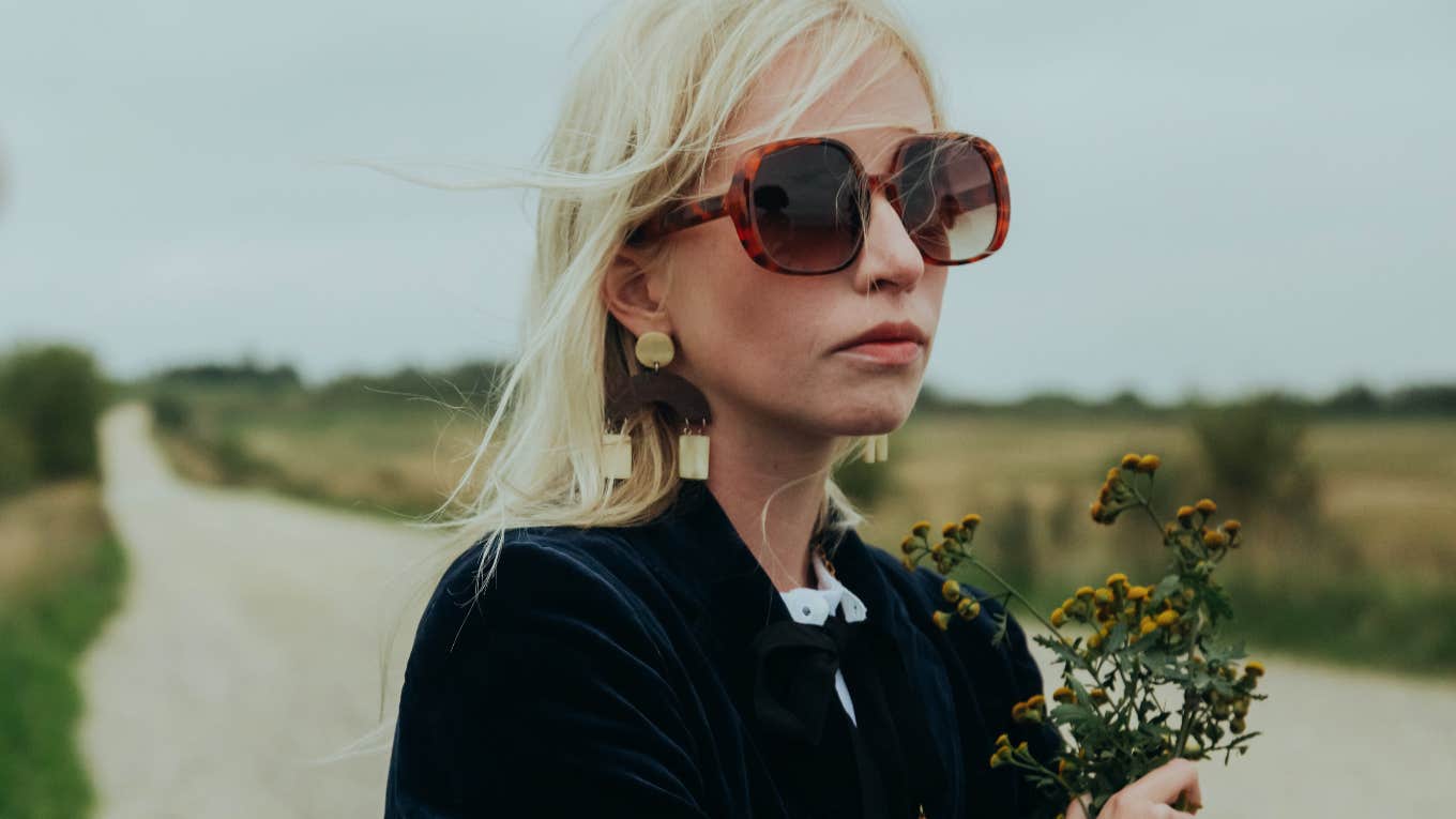 sad woman wearing sunglasses holding flowers