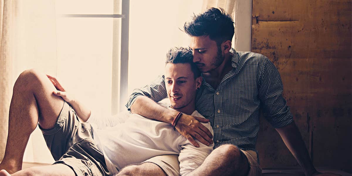two men cuddle romantically in front of a window