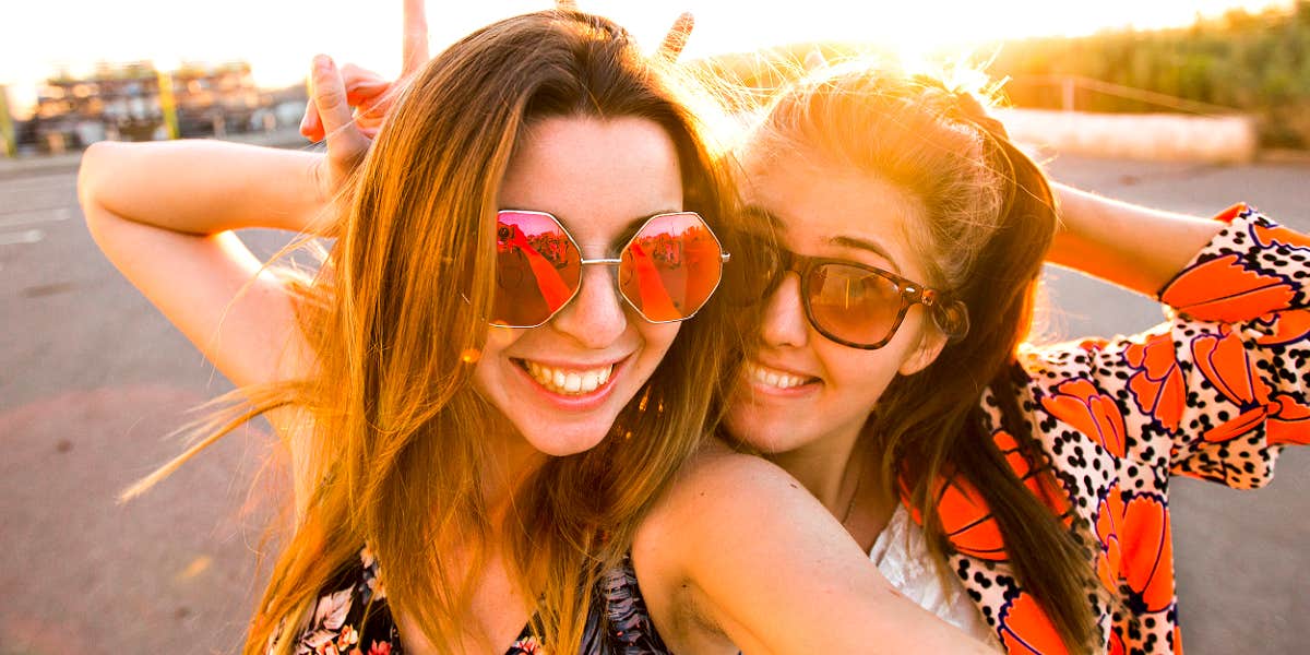 Two fun women smiling with the sun behind them, wearing wild glasses
