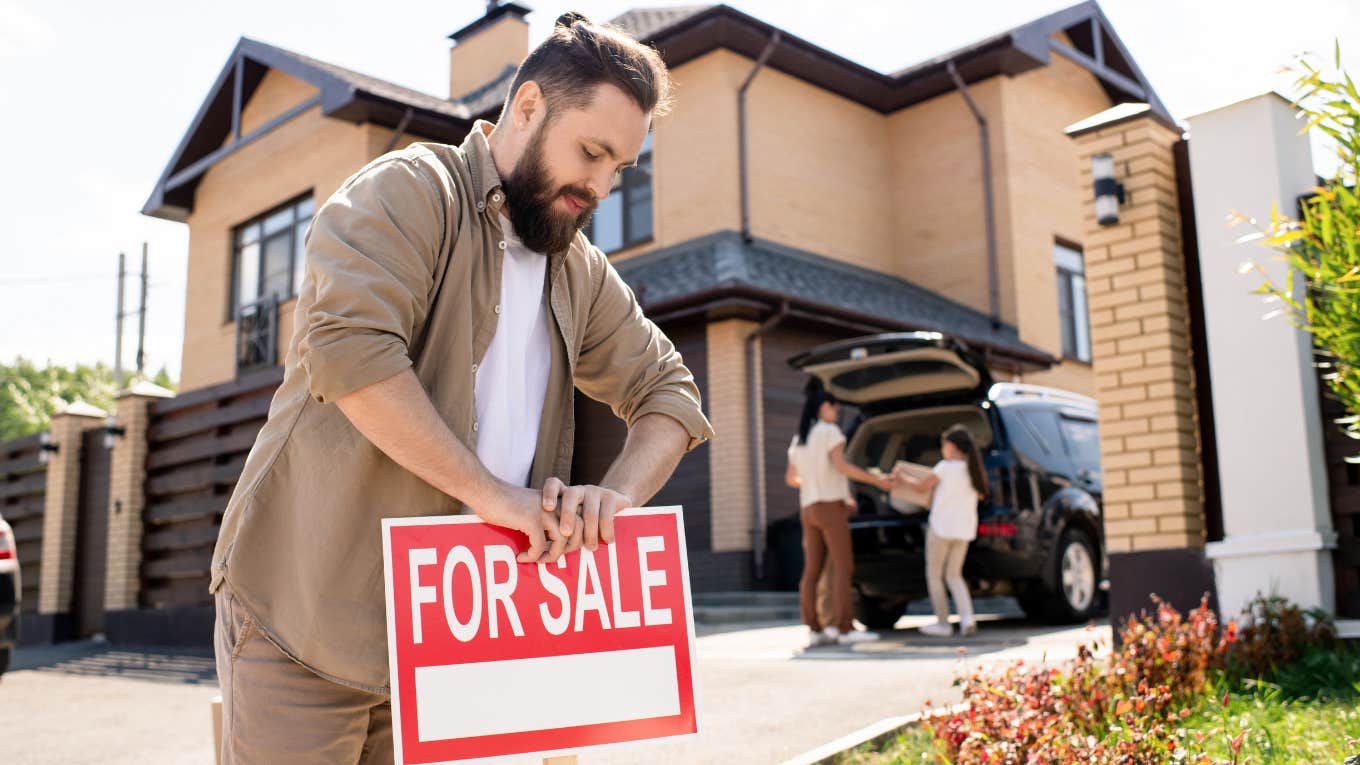 man putting out for sale sign in front of house
