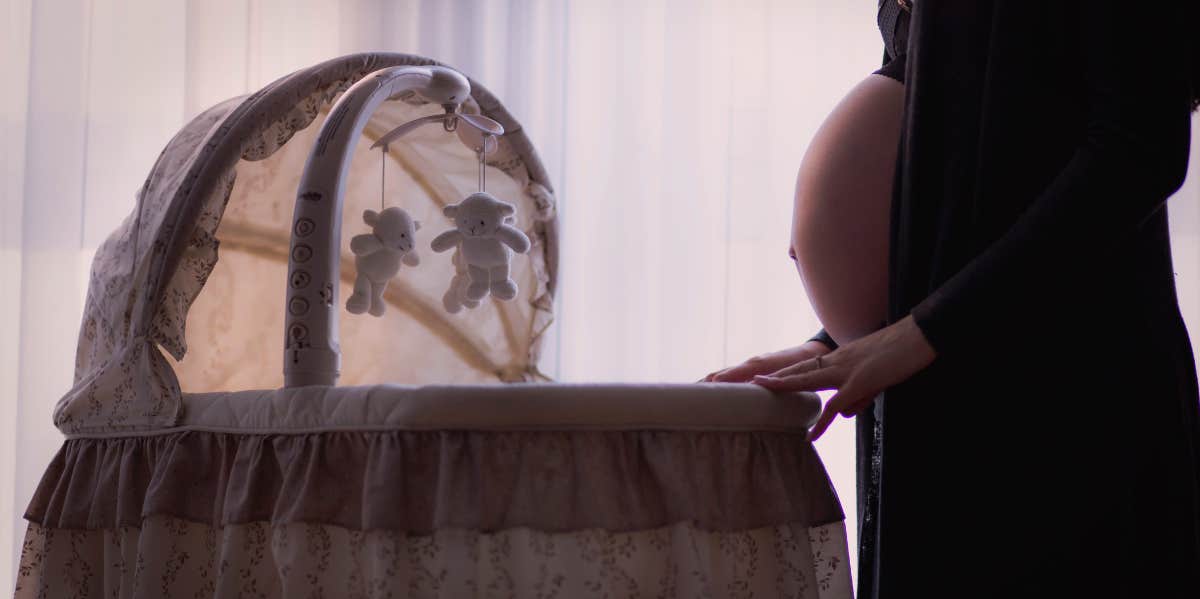pregnant person standing over a crib