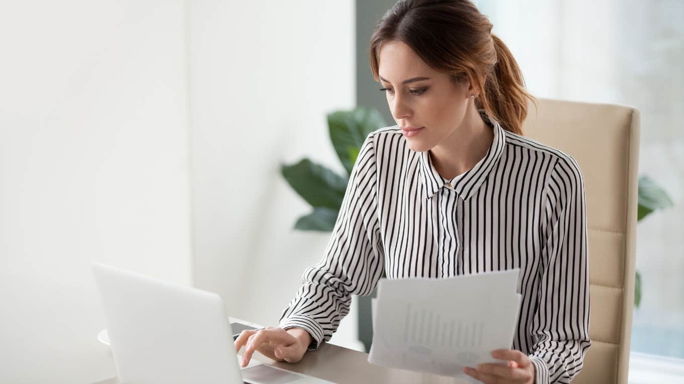 focused businesswoman typing on laptop and holding papers while sitting in office