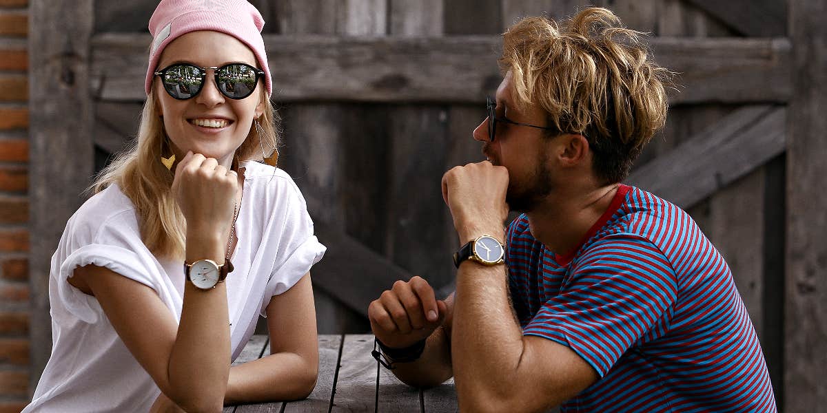 Couple sitting at a picnic table, him looking at her, she is smiling