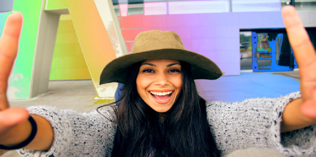 35 Best Cheesy Love Songs Of All Time woman taking selfie rainbow background smiling cheesy
