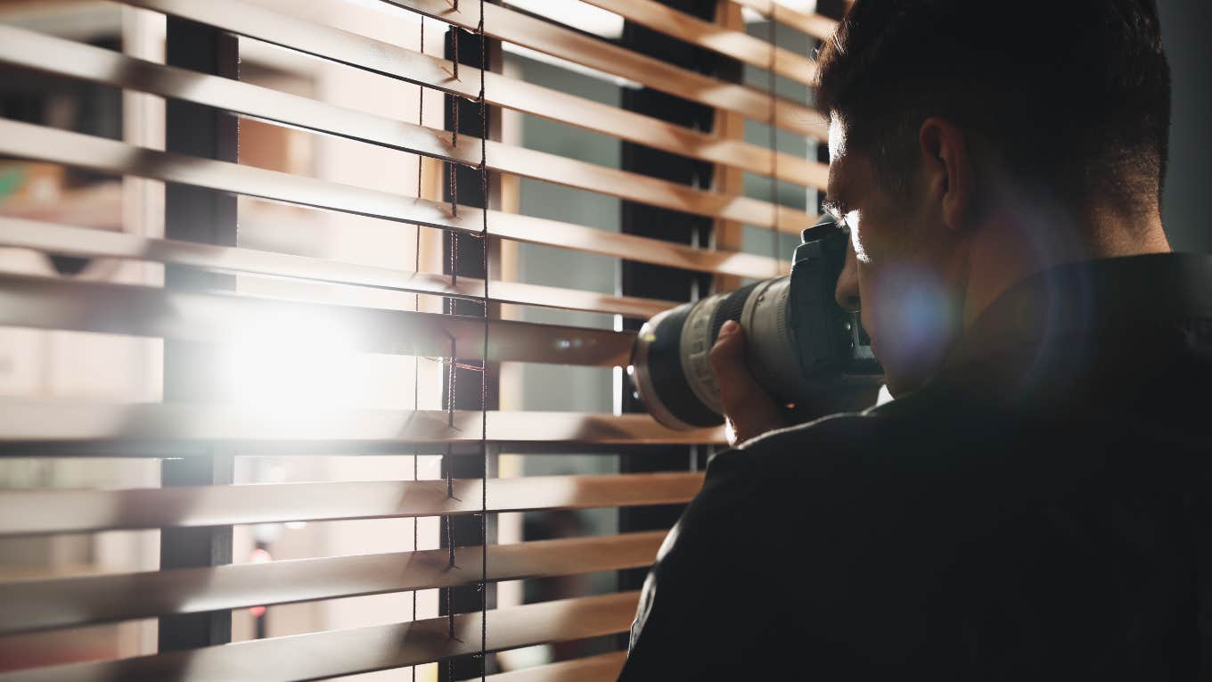 private detective with camera spying near window indoors