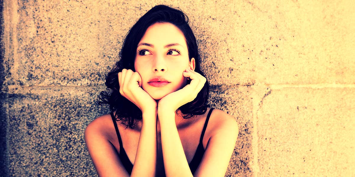 brunette woman sitting against brick wall looking thoughtful