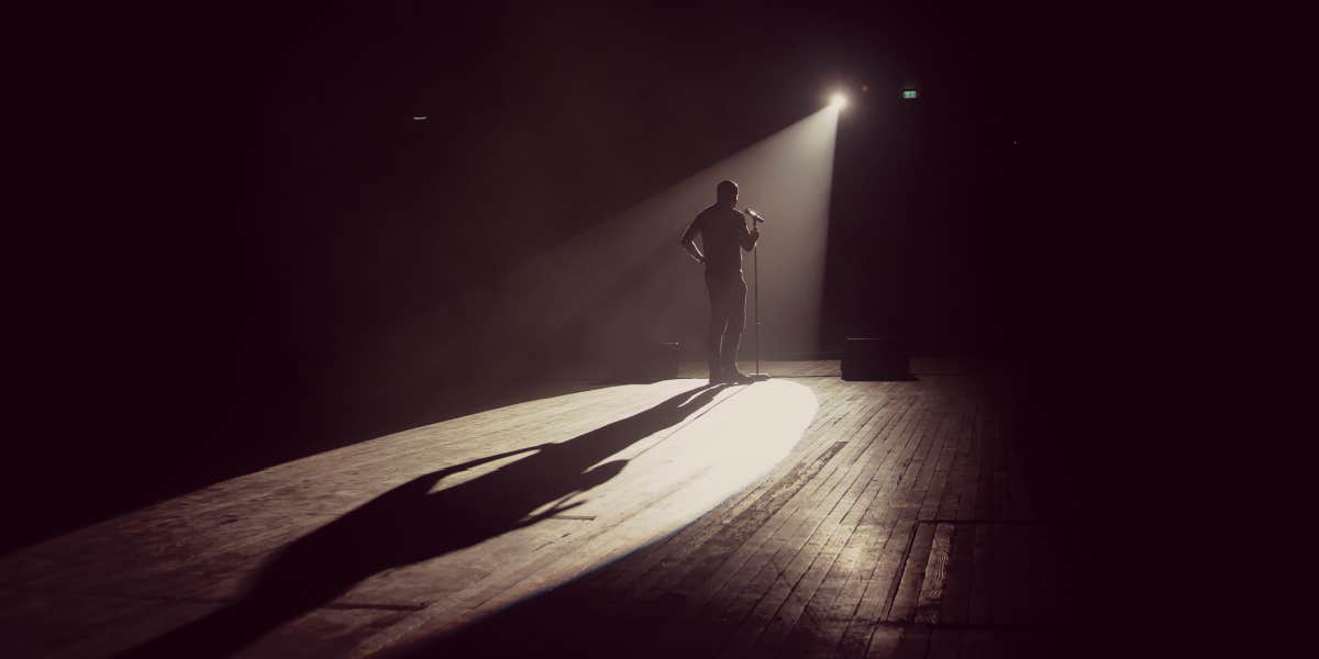 man on a stage doing comedy, backlit by spotlight 