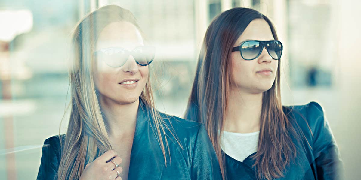 Two women in leather jackets looking in a reflective window, serious 